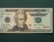 Detailed digital photograph of a modern U.S. twenty-dollar bill featuring Andrew Jackson's portrait, clear serial numbers, security features, and engraved design elements against a dark green background.
